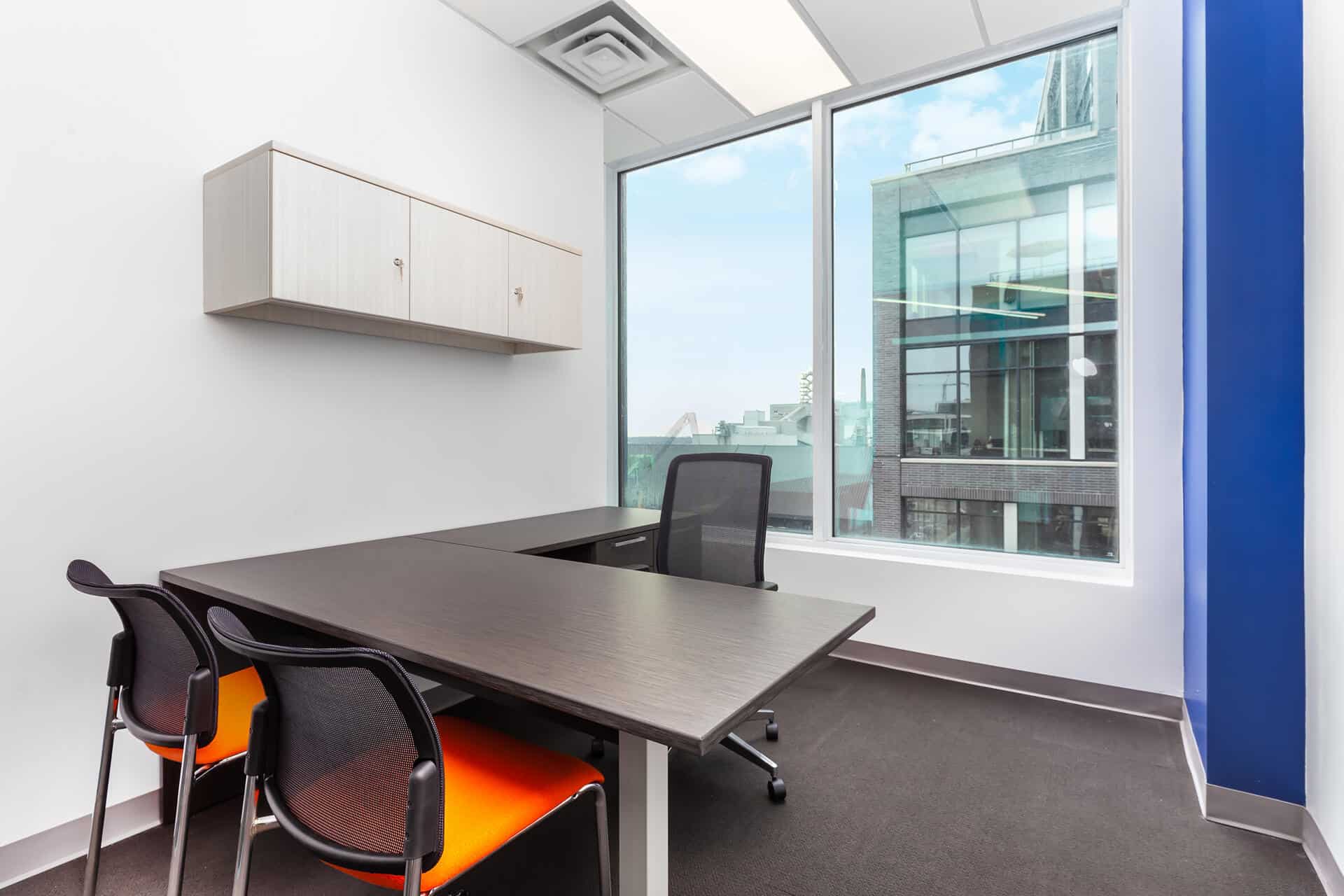 Modern office room with a large desk, two chairs, a wall cabinet, and a window with an urban view.