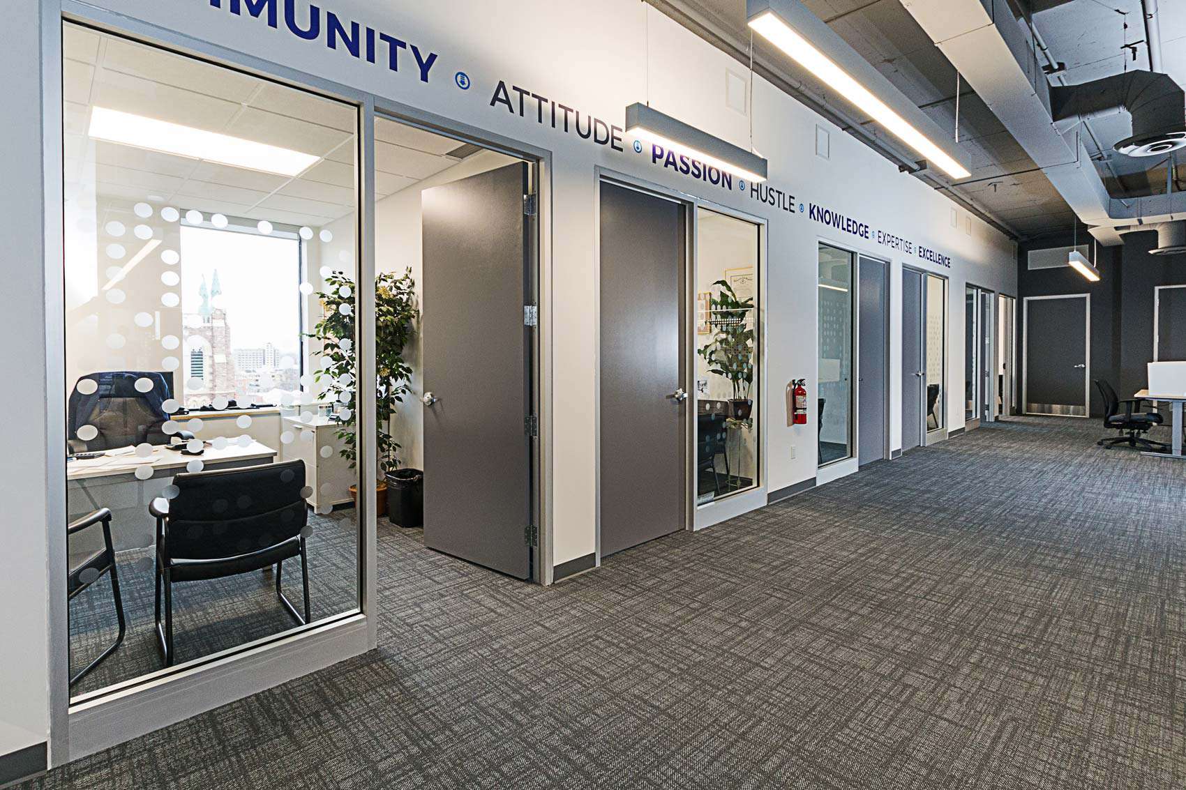 Modern office corridor with glass doors, motivational words on walls, and city view through the windows.