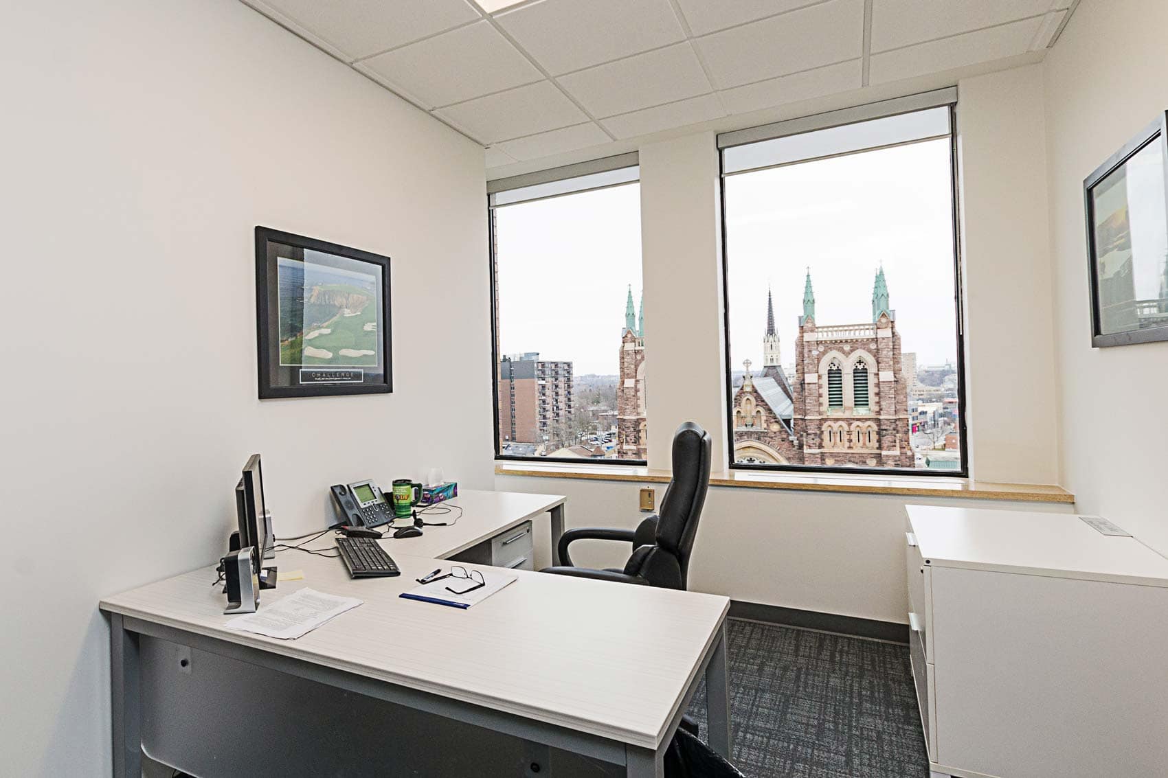 Modern office space with a desk, computer, office chair, and a window view of a cathedral.