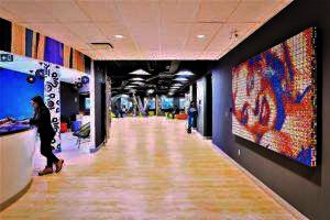 A vibrant office lobby with colorful decor, modern digital art on the walls influenced by lab accreditation themes, and people walking and working at reception desks.