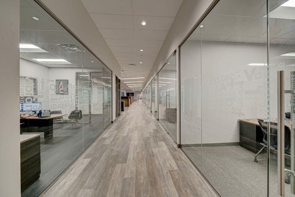 An image of a hallway with grey wood flooring and glass walls