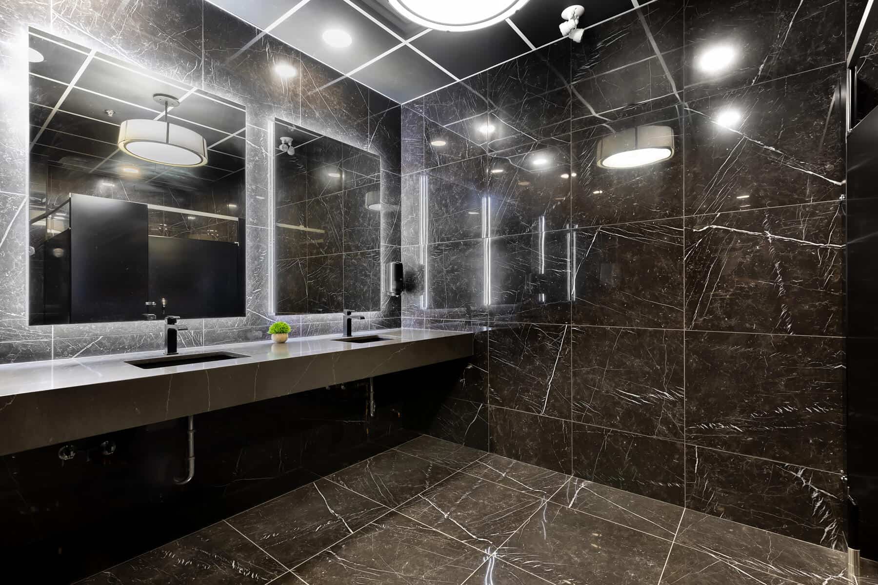 Modern bathroom interior with dark marble walls and floor, featuring a large mirror, double sink vanity, and stylish overhead lighting.