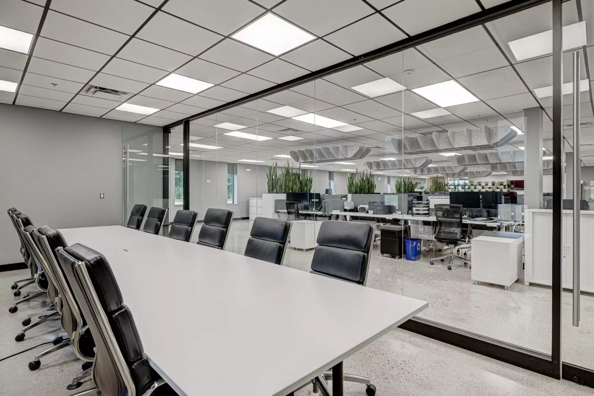 Modern office interior with a long conference table, black chairs, glass partitions, and multiple workstations in the background.