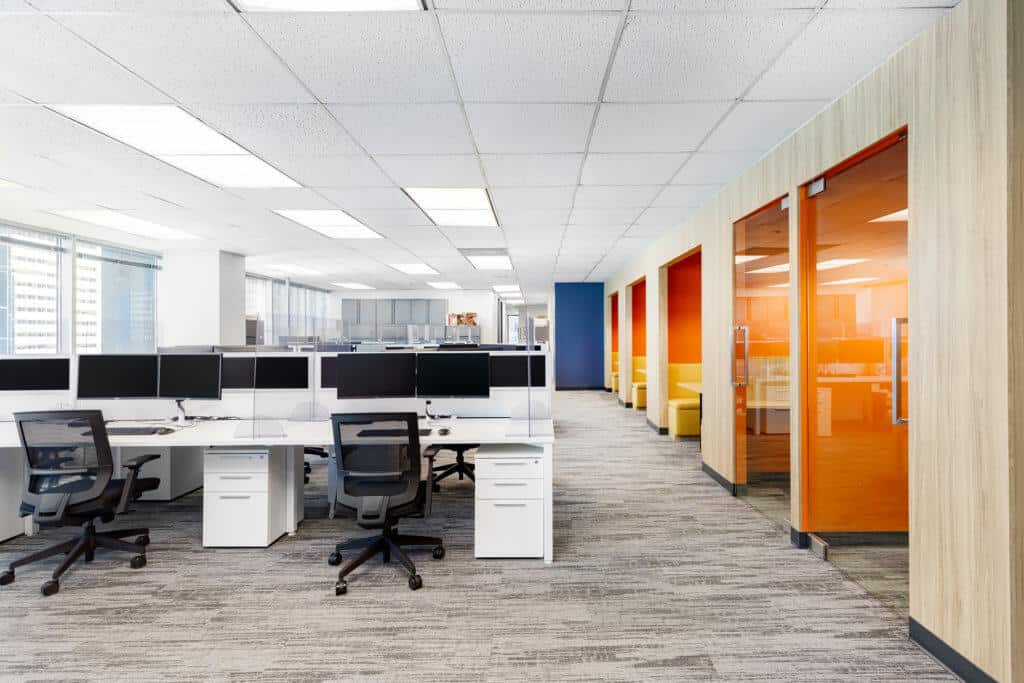 A view down an office walkway with an open office on the left and meeting booths on the right