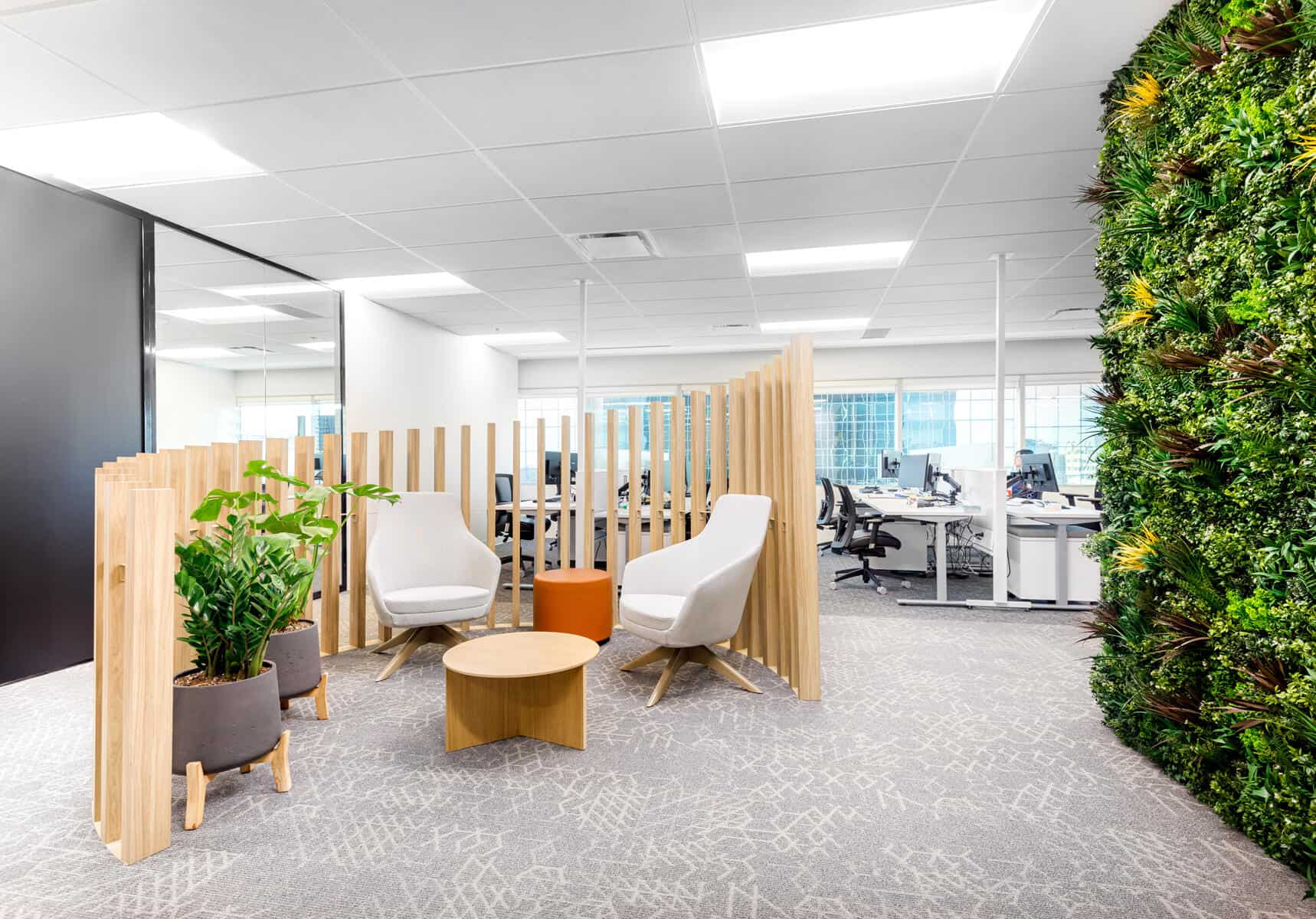 Office renovation featuring a modern interior with a seating area that includes white chairs, wooden partitions, a green living wall, and desks with computers in the background.