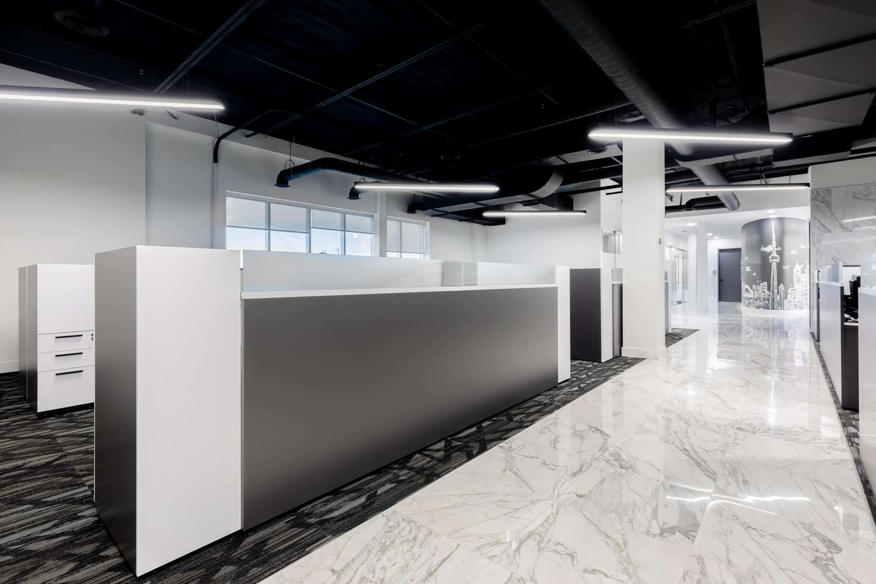 Modern office interior with sleek white desks and marbled floors, under a ceiling with exposed black ductwork and linear lighting.