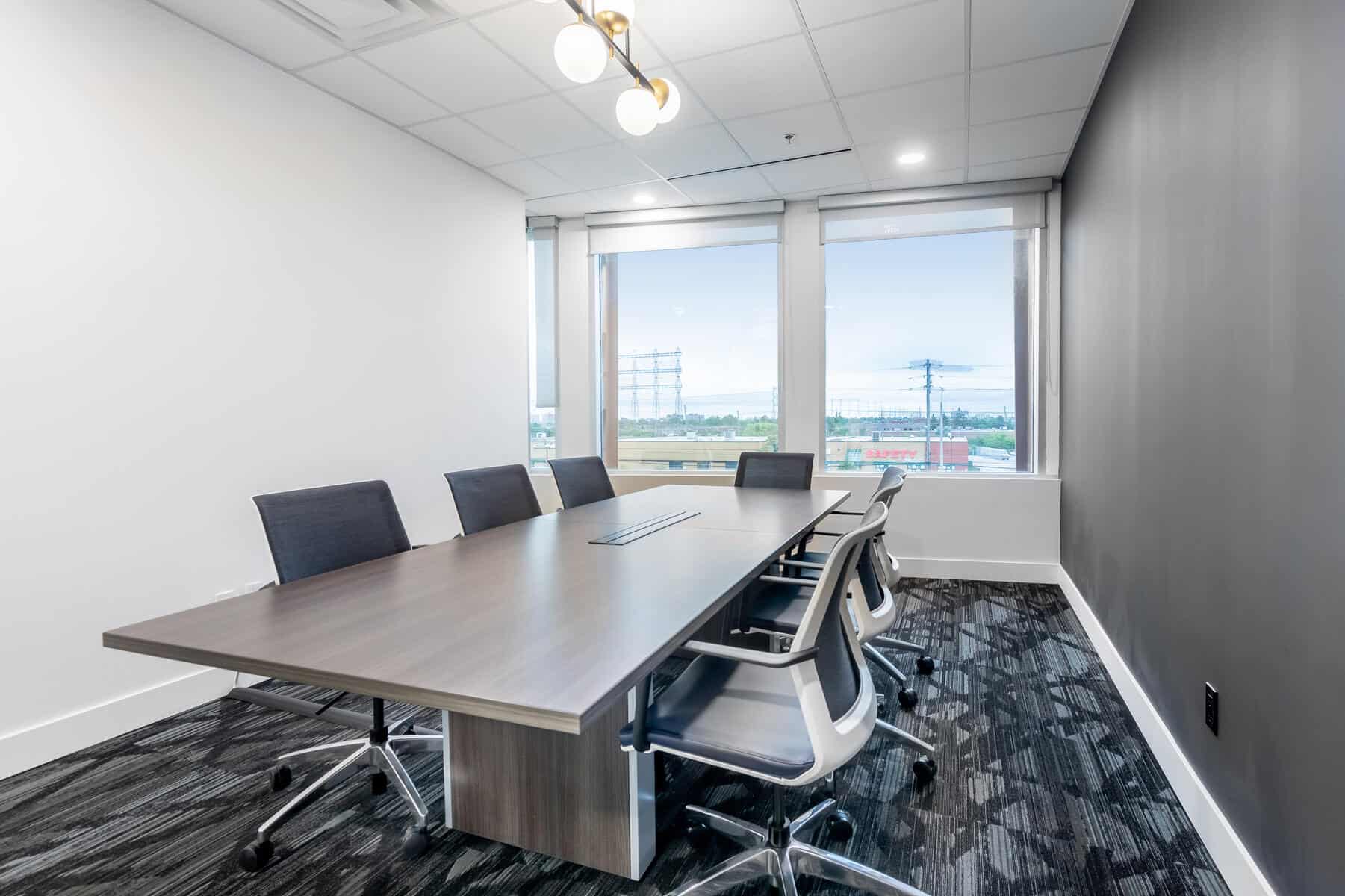 Modern office meeting room with a long table, chairs, and large windows showing an exterior view.