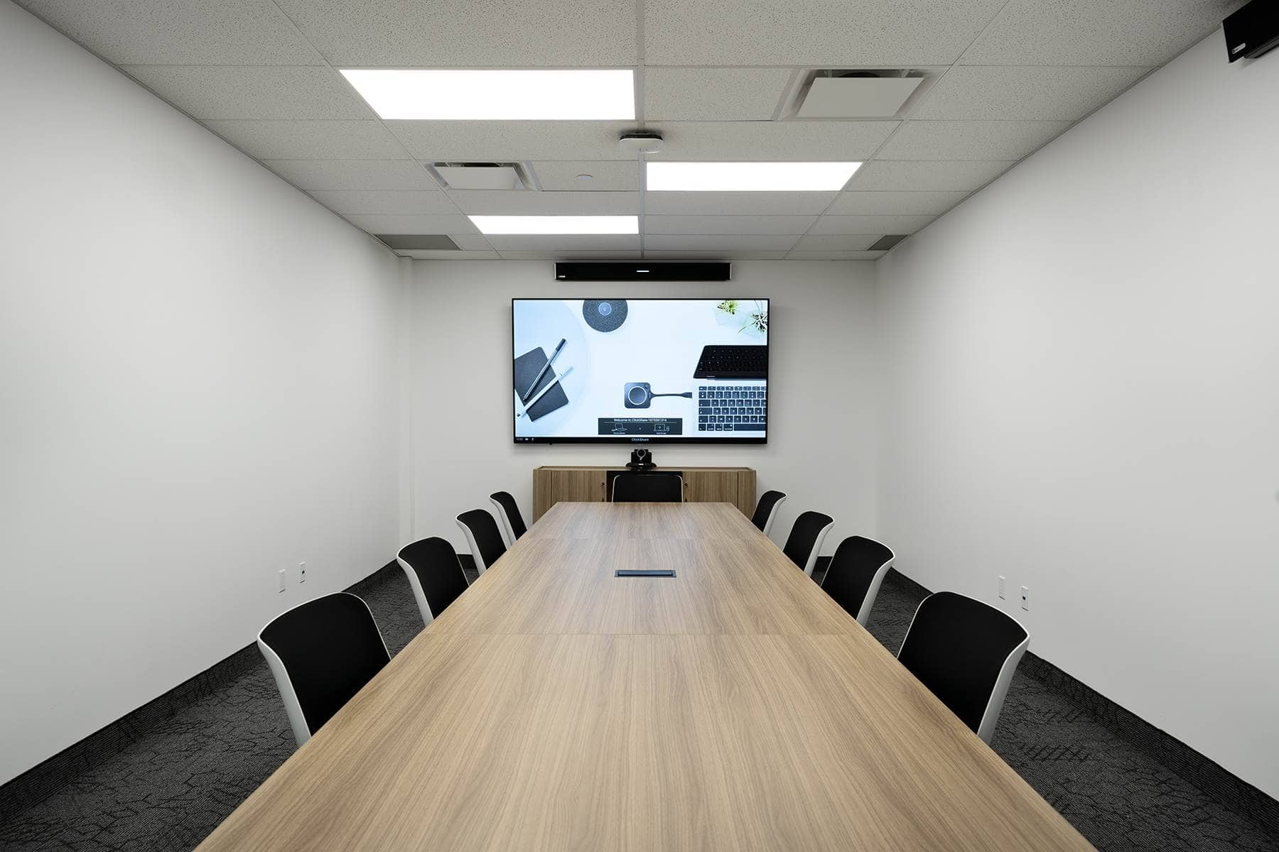 Modern conference room featuring a long table with chairs and a monitor displaying office tools on the wall at the end.