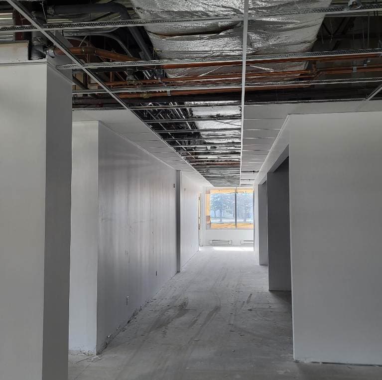 View of a new long corridor under construction with exposed ceiling infrastructure and unfinished drywall.