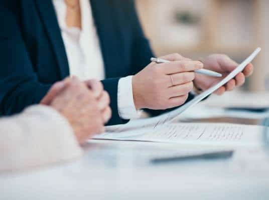 Two business professionals reviewing documents and using a digital tablet at a desk for graphic design.