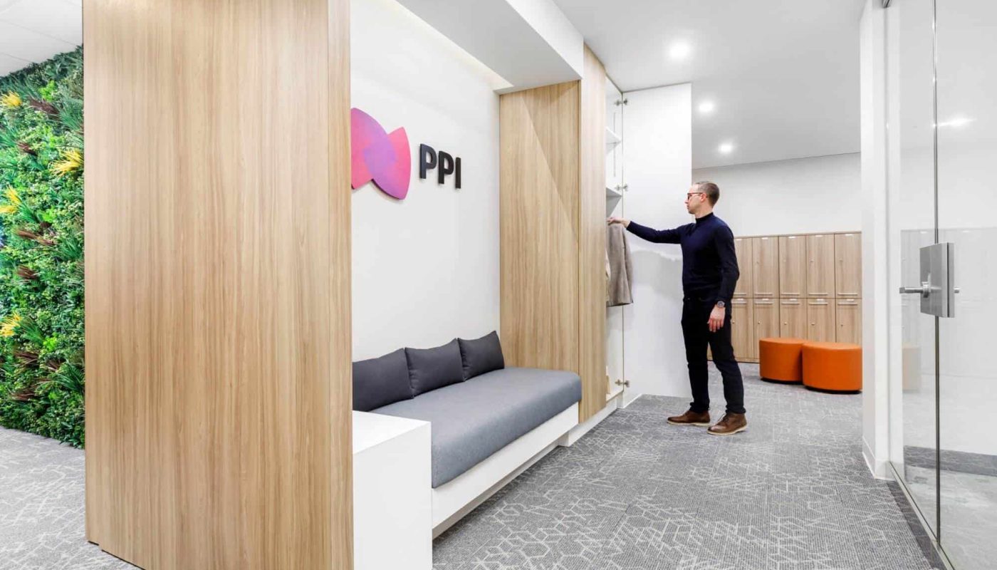 A man in a business casual outfit opening a sliding door in a modern office lounge with a green wall and graphic design company logo.