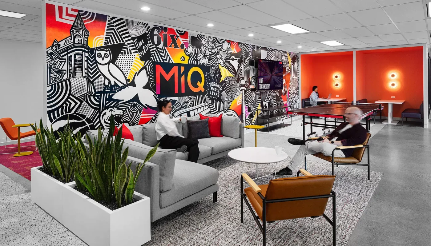 Modern office lounge with colorful graffiti mural, gray sofas, people sitting and chatting, a ping-pong table in the back, and contemporary decor.