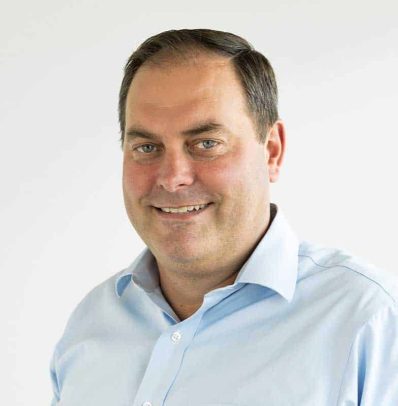 A smiling man in a light blue shirt poses against a plain white background for the new teams page.